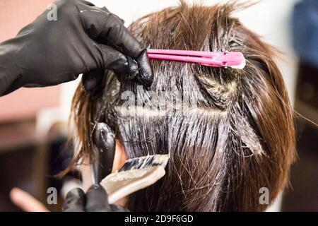 Gros plan de la coiffeuse appliquant un colorant chimique sur les cheveux Banque D'Images