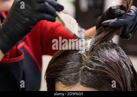 Gros plan de la coiffeuse appliquant un colorant chimique sur les cheveux Banque D'Images