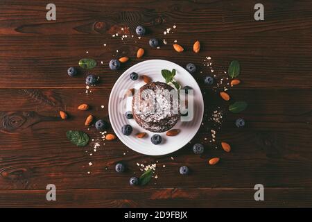 Chocolat muffin brownie sur plaque blanche parmi les bleuets et les amandes épars sur table en bois, vue du dessus. Banque D'Images