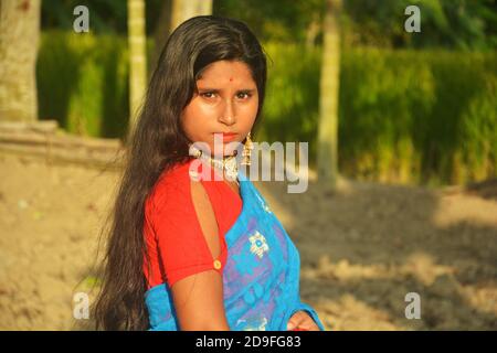 Gros plan d'une jeune fille bengali indienne, portant un sari bleu avec des cheveux longs et une pointe de nez dorée, des boucles d'oreilles, un collier dans un champ labouré, un foyer sélectif Banque D'Images