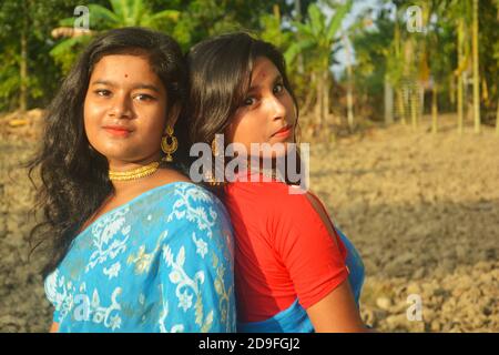 Gros plan de deux belles filles indiennes adolescentes bengali portant sari et bijoux dorés comme collier boucles d'oreilles nez broche et debout dos à dos Banque D'Images