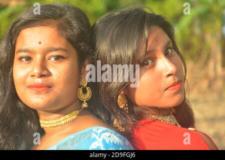 Gros plan de deux belles filles indiennes adolescentes bengali portant sari et bijoux dorés comme collier boucles d'oreilles nez broche et debout dos à dos Banque D'Images