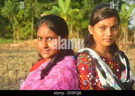 Deux belles filles indiennes adolescentes bengali portant sari salwar kameez et bijoux dorés comme boucles d'oreilles nez broche et debout dos vers l'arrière Banque D'Images