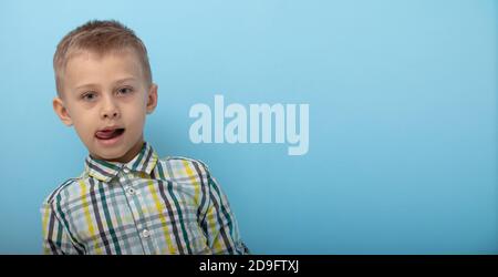 un garçon dans une chemise à carreaux pose sur fond bleu. l'enfant montre des émotions sur la caméra. concept de formation et de préparation à l'école Banque D'Images