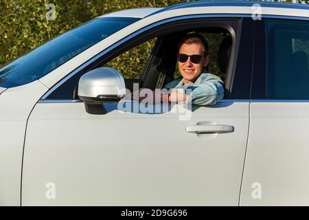 Guy en veste en denim et lunettes noires sourit à la roue d'une voiture Banque D'Images