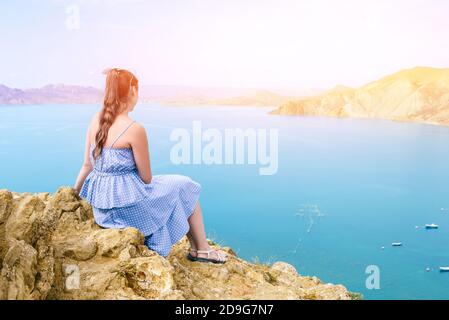 Fille dans une robe bleue se trouve sur la montagne et admire le paysage marin. Le voyageur regarde les montagnes et la mer. Randonnée, aventure et actif Banque D'Images