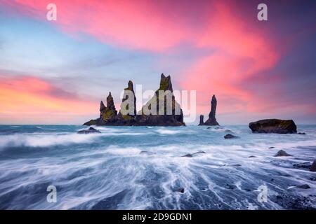 Formations rocheuses de basalte Troll toes sur la plage noire avec des nuages roses de coucher de soleil. Grand ciel violet brillant sur fond. Reynisdrangar, Vik, Islande Banque D'Images