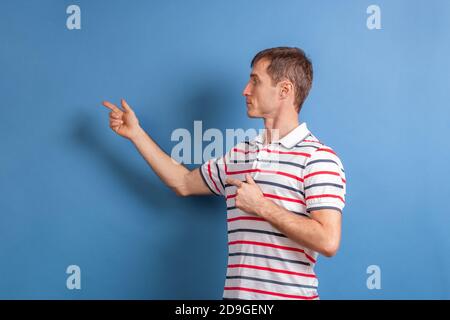 Un professeur de sexe masculin montre quelque chose sur le mur sur un fond bleu. Jeune gars pointe son doigt sur le texte publicitaire. Banque D'Images