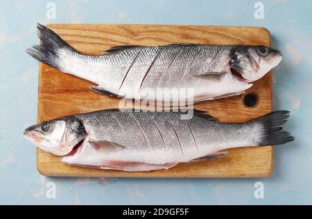 Poisson frais de mer cru sur la planche en bois de coupe sur fond bleu. Gros plan. Vue de dessus. Format horizontal Banque D'Images