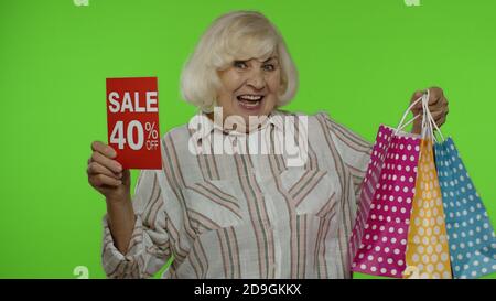 Grand-mère gaie avec des sacs d'achats montrant la vente 40 pour cent de rabais sur la publicité de texte de bannière. Achats en ligne à bas prix le Black Friday. Femme âgée se réjouissant de rabais sur les soldes de vacances Banque D'Images