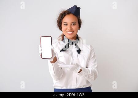 Belle hôtesse afro-américaine avec téléphone mobile sur fond gris Banque D'Images