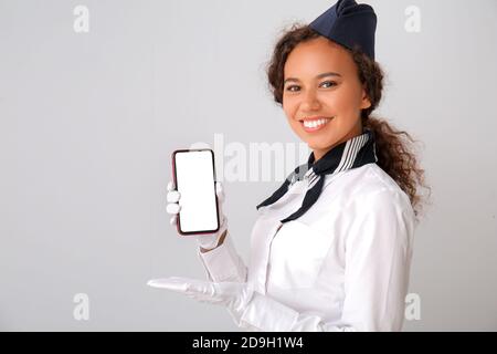 Belle hôtesse afro-américaine avec téléphone mobile sur fond gris Banque D'Images