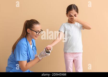 Médecin vérifiant le taux de sucre dans le sang de la fille diabétique sur la couleur arrière-plan Banque D'Images