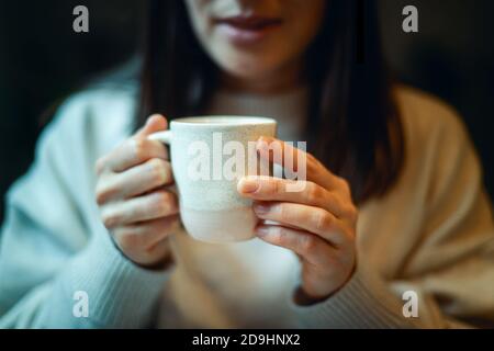 Jeune femme en chandail chaud tenant une tasse de café et planant des objectifs personnels pour la nouvelle année. Banque D'Images