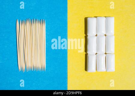 cure-dents sur fond bleu et gommes à mâcher en groupe dans un contenant blanc sur fond jaune, vue du dessus Banque D'Images