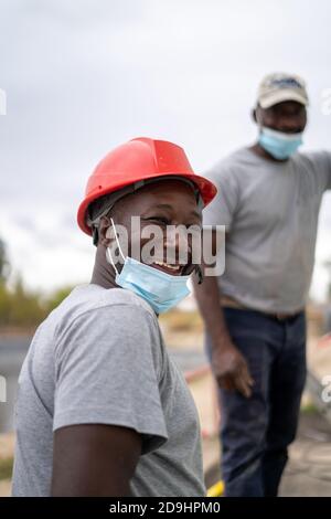 Les constructeurs afro-américains portant des casques et des masques de protection au travail Banque D'Images