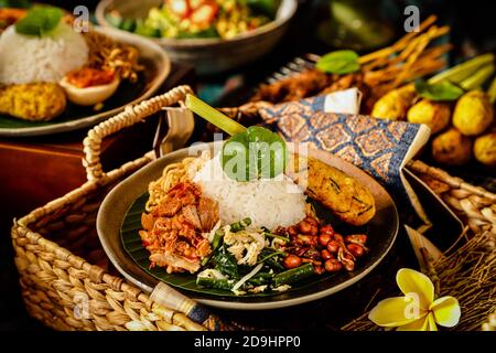 Nasi Campur Bali. Repas balinais de riz avec poulet râpé, salade de légumes, arachides, satay, œuf et nouilles frites. Banque D'Images
