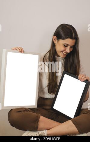 Photo verticale d'une femme charmante et décontractée qui en tient deux cadres vides de tailles différentes Banque D'Images