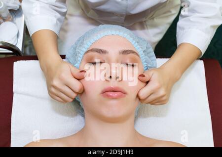 Le cosmétologue du masseur effectue une procédure de rajeunissement de la peau du visage à l'aide d'un massage manuel. Vue de dessus gros plan Banque D'Images