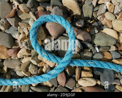Boucle simple de corde bleue couchée sur des galets de plage Banque D'Images