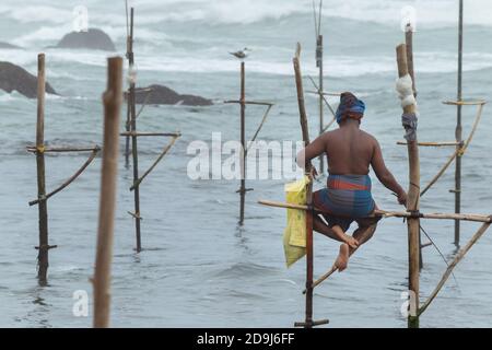 Pêcheur de stilt avec sa tige en bois face à l'arrière de l'appareil photo sans un sommet, la pêche dans une méthode traditionnelle unique dans la culture sri lankaise, soupir ensoleillé Banque D'Images