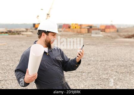 Un ingénieur de bâtiment américain tient un talkie-walkie VHF et des papiers sur le chantier de construction. Banque D'Images