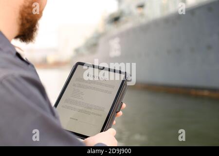 Un ingénieur maritime lit le contrat sur une tablette près du navire en arrière-plan. Banque D'Images