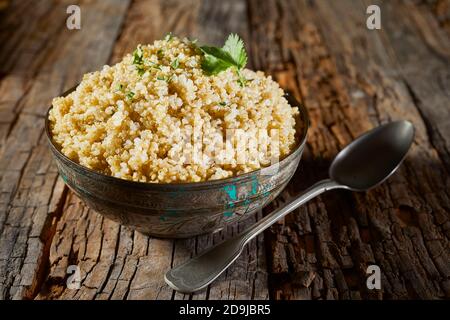 Couscous et quinoa sains assaisonnés avec des herbes servies dans un grand bol rustique sur une ancienne table en bois pour les végétariens et cuisine végétalienne Banque D'Images