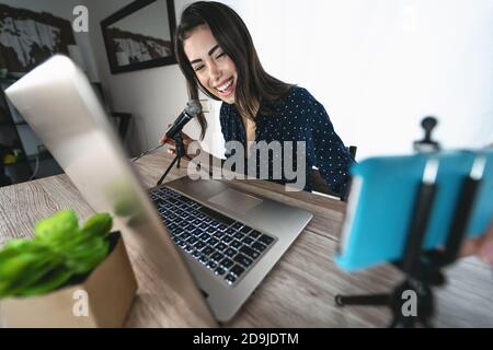 Bonne femme filmant un podcast vidéo avec l'appareil photo de smartphone pendant Utilisation de l'ordinateur - jeune fille s'amusant dans la diffusion en direct sur les réseaux sociaux Banque D'Images