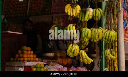 Katmandou, Népal - 11/11/2019: Vendeur à peine visible dans l'ombre dans une boutique de fruits avec des bananes suspendues en face dans le quartier touristique de Thamel. Banque D'Images