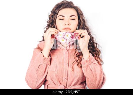 Jeune belle femme en costume rose sur fond blanc. Elle porte un masque protecteur de fleurs en fleur sur son visage. Respirez de l'air frais. Air contaminé Banque D'Images