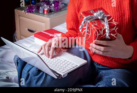 Vue de dessus d'une main féminine tenant une boîte cadeau et saisissant du texte sur un ordinateur portable. Salutations en ligne pour Joyeux Noël et bonne année Banque D'Images