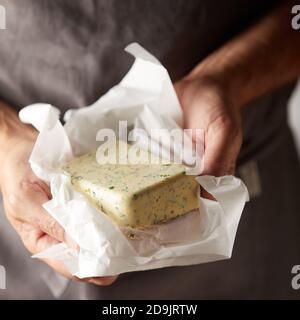 Mains d'un chef tenant une pat de beurre d'herbes ouvrir dans son enveloppe en vue rapprochée Banque D'Images