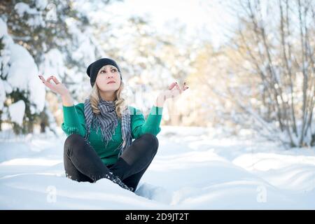 Belle femme est assise en position lotus dans le parc gelé. Concept de tranquillité et de yoga avec espace copie. Banque D'Images