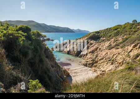 Une petite plage de sable et turquoise méditerranéen dans un endroit isolé crique rocheuse sous un ciel bleu près d'Ostriconi dans le Balagne région Corse Banque D'Images