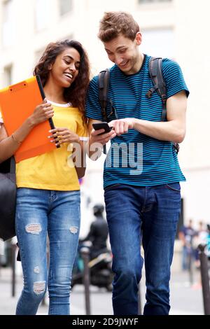 Portrait des étudiants d'université heureux, hommes et femmes, qui marchent en ville regarder un téléphone mobile Banque D'Images