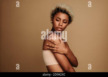 Portrait d'une femme afro-américaine sur fond marron. Femme aux cheveux bouclés debout avec le bras croisé en regardant au-dessus de l'épaule. Banque D'Images