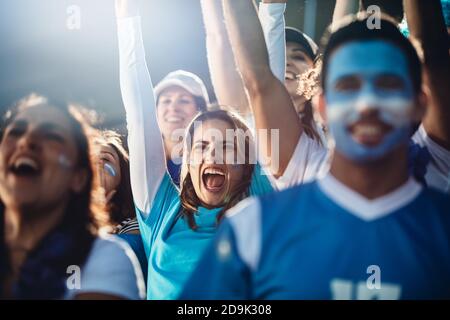 Femme Argentine avec un groupe de fans de football acclamer dans le stade. Une foule de fans de football applaudissent leur équipe tout en regardant un match au stade. Banque D'Images