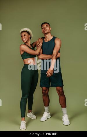 Couple en vêtements de fitness debout ensemble sur fond vert. Bonne forme physique femme debout avec un athlète masculin. Banque D'Images