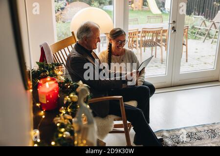 Homme et femme senior à la maison pendant Noël ayant un appel vidéo sur leur tablette numérique. Un couple senior appelle sa famille par vidéo via une tablette informatique Banque D'Images