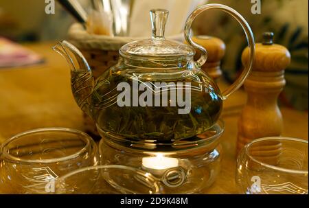 Théière en verre transparent avec thé vert sur le brûleur dans un cadre confortable. Thé. Un café. Banque D'Images