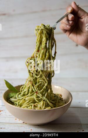 Mains servant des pâtes dans une sauce pesto provenant d'un bol Banque D'Images