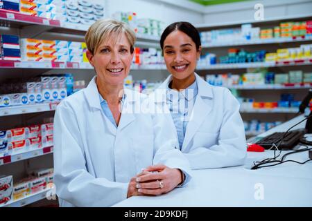 Le directeur de pharmacien caucasien et l'assistante féminine de race mixte souriant pendant debout en pharmacie Banque D'Images