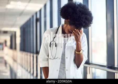 Triste et déprimé jeune femme afro-américaine médecin en blanc uniforme dans le couloir Banque D'Images