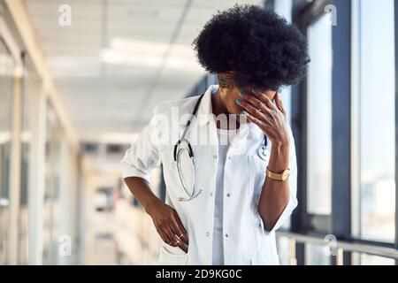 Triste et déprimé jeune femme afro-américaine médecin en blanc uniforme dans le couloir Banque D'Images