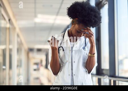 Triste et déprimé jeune femme afro-américaine médecin en blanc uniforme dans le couloir Banque D'Images