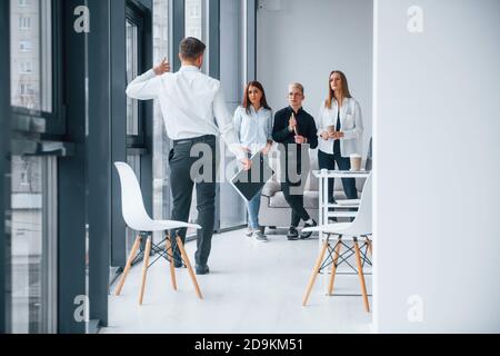 Homme en vêtements formels marchant et parlant. Groupe de jeunes succès équipe qui travaillent et communiquent ensemble à l'intérieur dans le bureau Banque D'Images