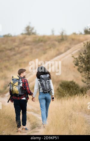 Vue arrière d'un couple multiethnique avec sacs à dos et porte-smartphone mains en marchant sur le chemin Banque D'Images