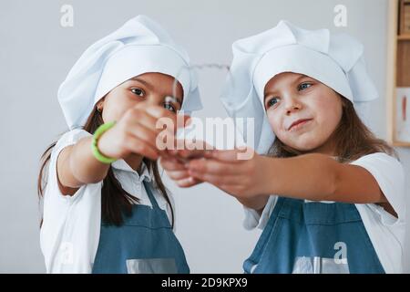 Deux petites filles en uniforme bleu de chef travaillant avec la farine sur la cuisine Banque D'Images