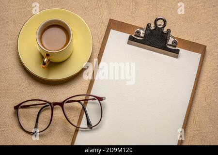 business desktop concept - presse-papiers avec papier vierge, lunettes de lecture et une tasse de café contre du papier texturé Banque D'Images